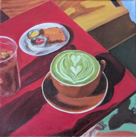 Matcha with bakery on table Tasse mit grünem Getränk und Herzmuster, kombiniert mit kleinen Speisen auf einem Tisch.